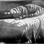 A man in bed is bathed in striped light