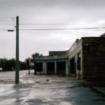 A sidewalk in front of store with telephone pole.