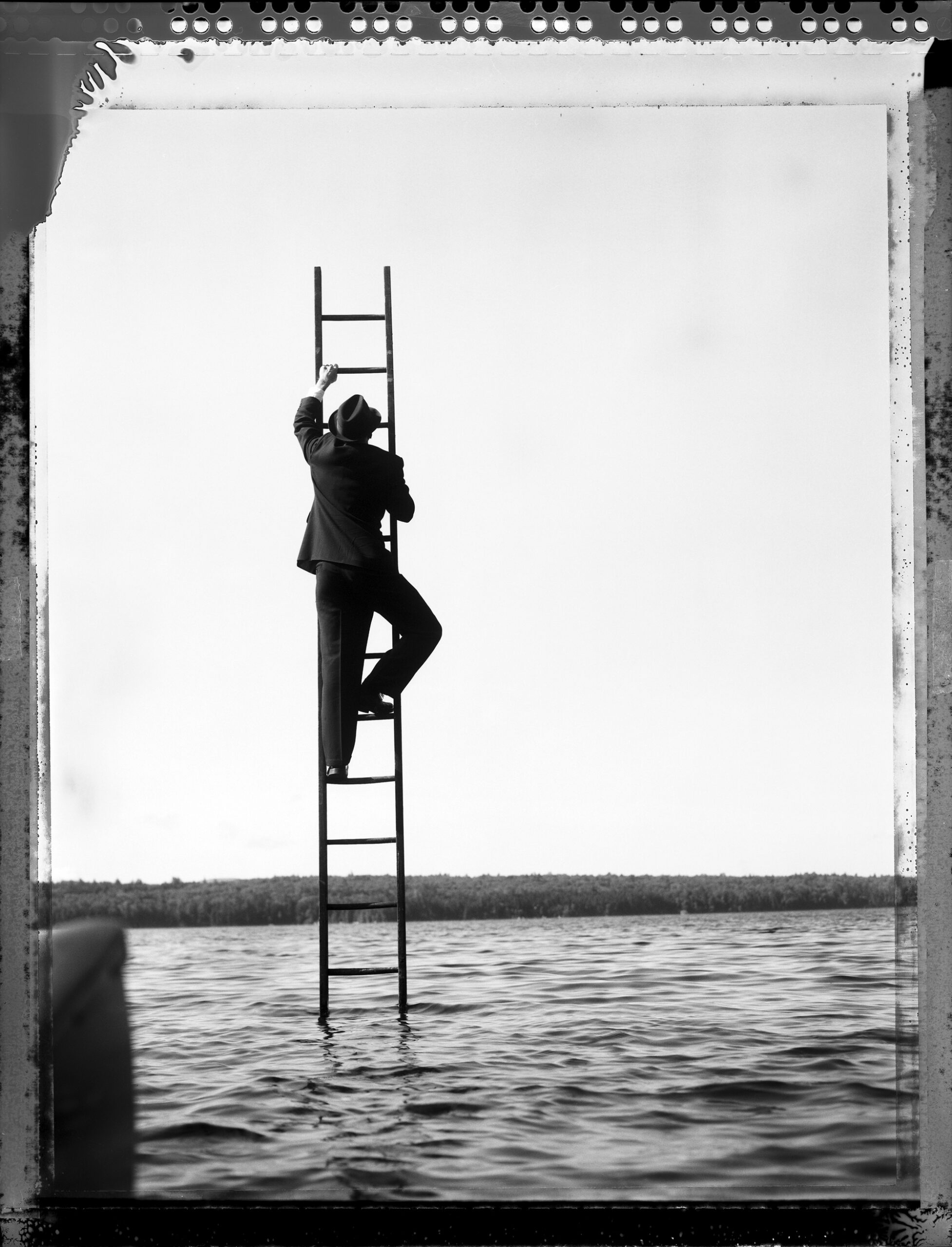 A man in a suit and hat on a ladder in the sea.