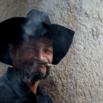 A man with a black cowboy hat and smoking