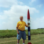 A man standing on a hillside with a rocket.