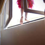 A woman stands on a window sill in a red skirt.