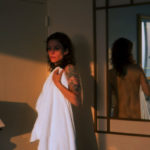 A woman stands with a towel and is reflected in a mirror.