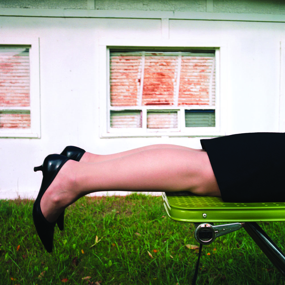 A woman lying on an ironing board with her legs stretched out with heels on.