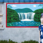 A wall with a waterfall mural with a cutout of a girl with braids.