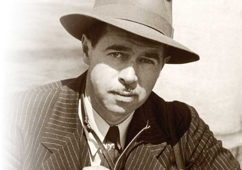 Portrait of Arthur Griffin. He wears a pin-striped shirt and a hat.