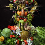 A man shape made out of fruit and flowers.