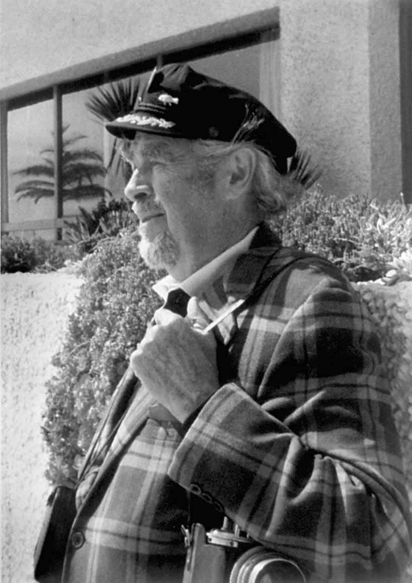 A portrait of Arthur Griffin with a cap and a camera over his shoulder.