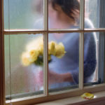 Woman holding yellow roses behind a window