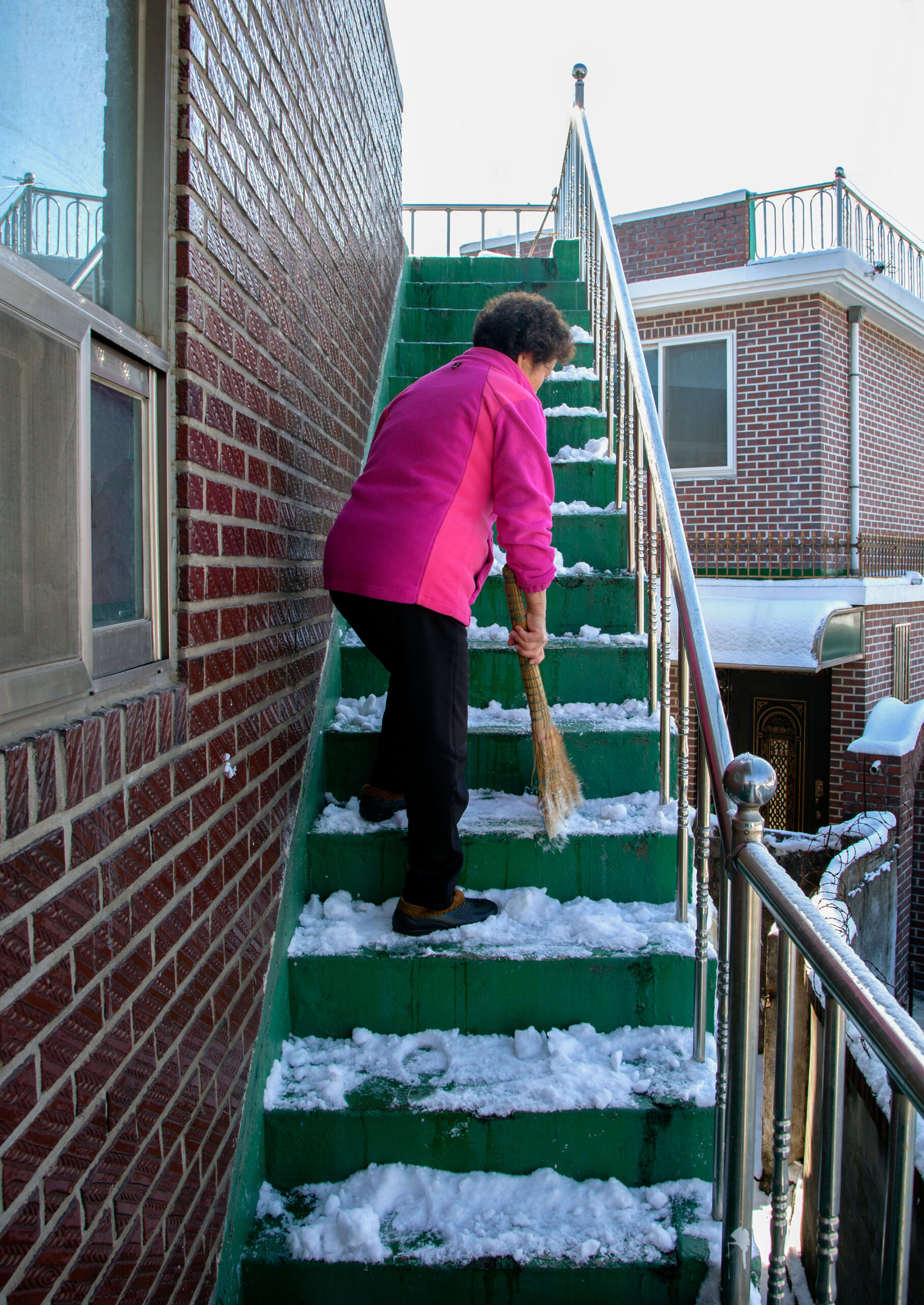 A woman sweeps snow off stairs.