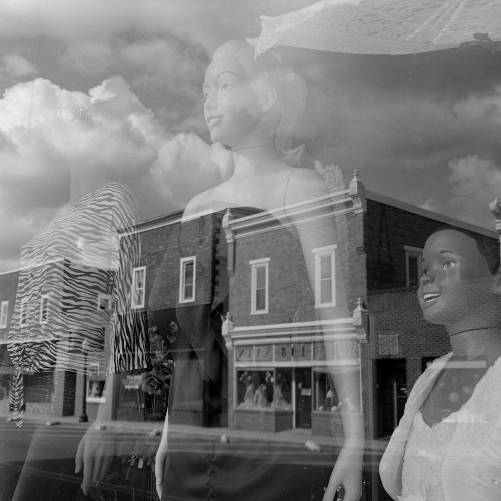 A window store front of mannequins reflects the buildings from across the street.