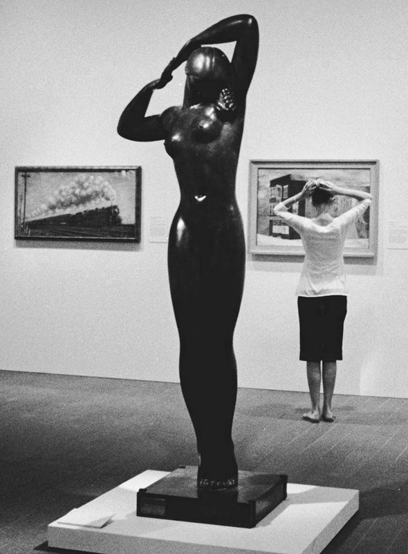 A women looks at a painting. The sculpture in from t of her mimics her hand gesture over her head