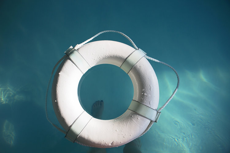 A white life saver floats on water and a person's foot is seen through the center from the bottom of the pool.
