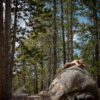 A nude woman lies on a boulder in the woods.