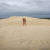 A nude woman stands in the sand of the desert.