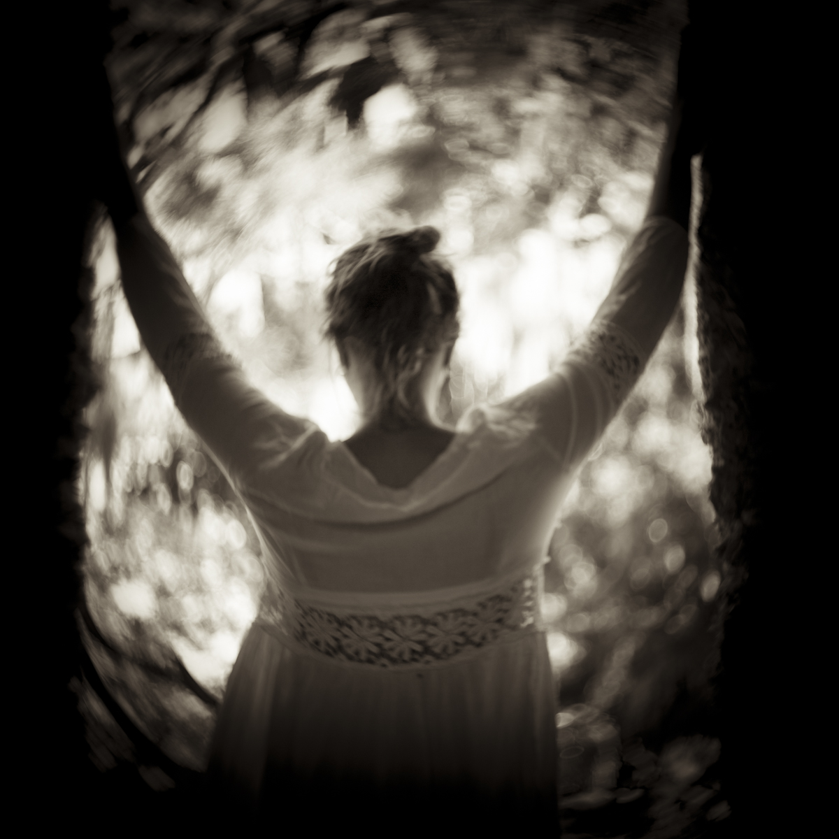 A woman holds her arms up and has her back towards us. A strong light makes a silhouette of her upper body.