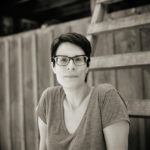 Portrait of a woman sitting on a wide ladder against a fence.