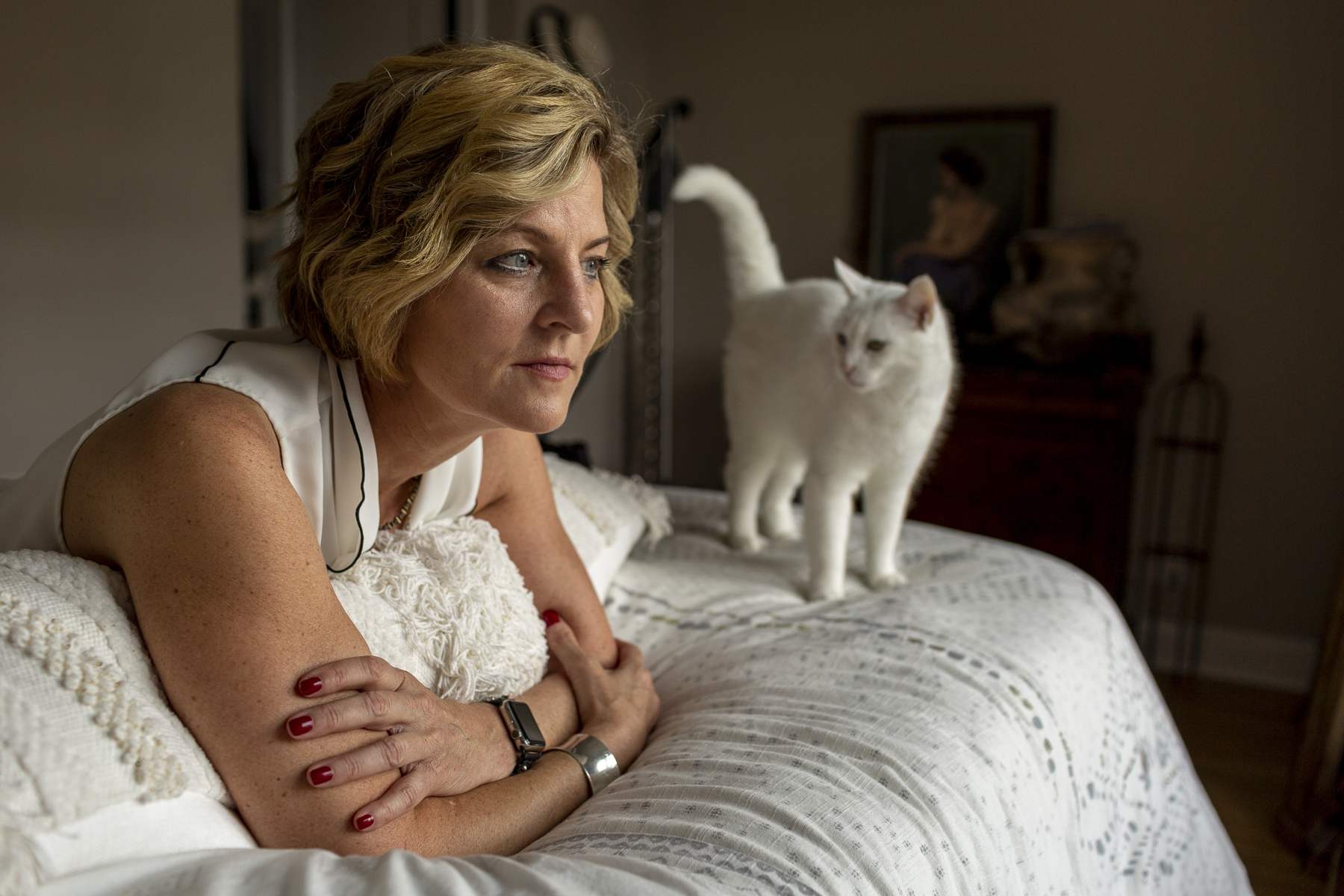 A woman lies on her bed with a white cat.