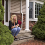 A woman sits on her front stoop of her house.