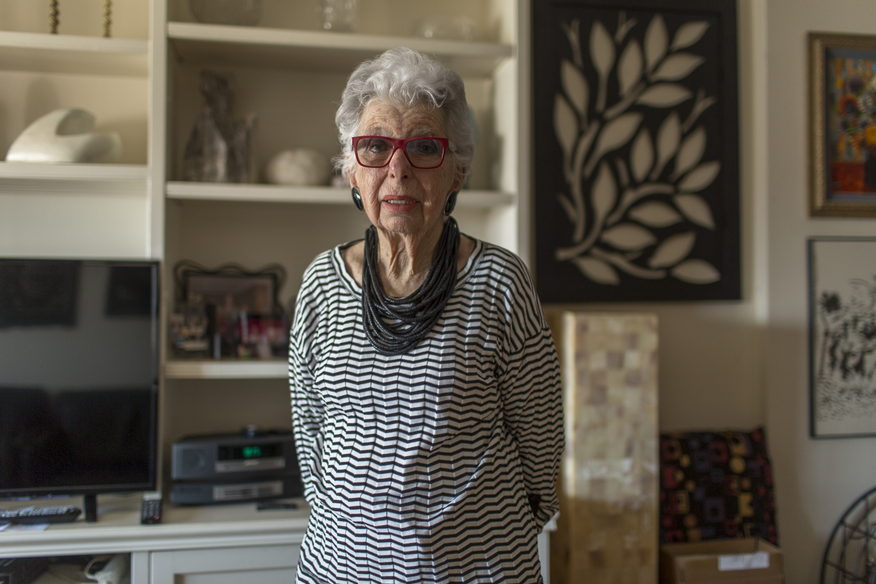 An older woman stands in her kitchen.