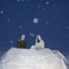 Two men soldiers build an igloo. The sky is dark blue.