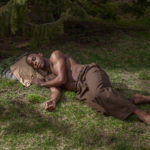 Man lays on the grass and rests his head on a boulder