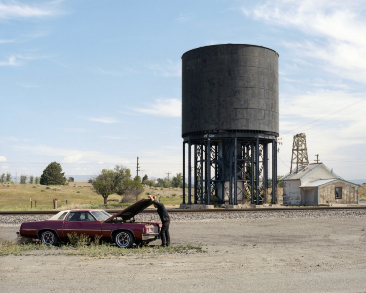 man fixing truck with water tower in background